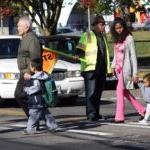 A group of students and families walk across the street as a crossing guard holds a stop sign to halt traffic